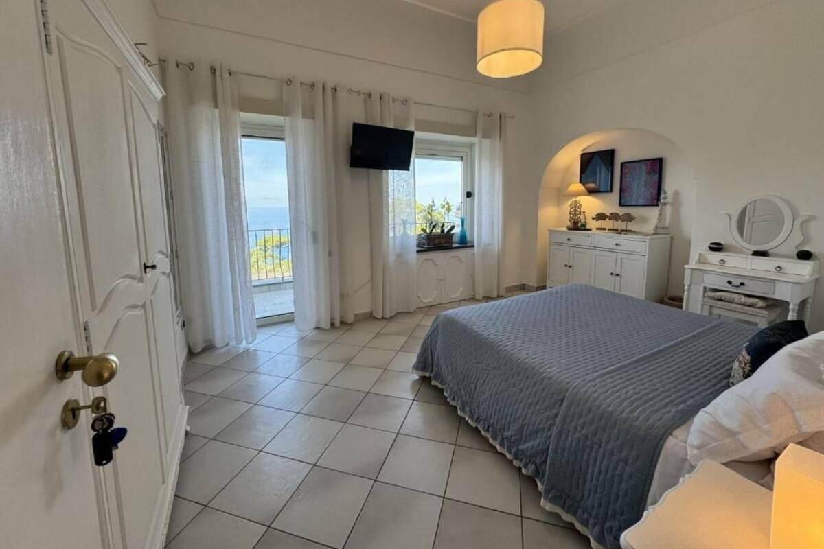 A bedroom with a bed, a TV mounted on the wall, a dresser, and a window with curtains.