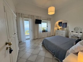 Ein Schlafzimmer mit einem Bett, einem an der Wand befestigten Fernseher, einem Schminktisch und einem Fenster mit Vorhängen.