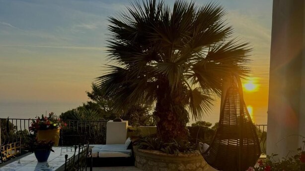 A terrace with a table, chairs, a lounge chair, and a palm tree. - Villa Azul (Anacapri)