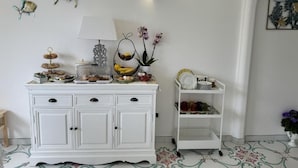 A white cabinet with drawers, a hanging basket, a lamp, and a small shelf with dishes. - Villa Azul (Anacapri)