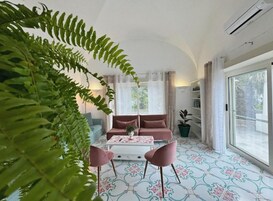 Ein Wohnzimmer mit einer Couch, einem Couchtisch, Stühlen, einem großen Fenster und einer Pflanze.