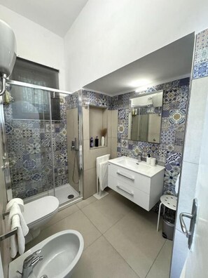 Casa de banho com chuveiro, sanita, lavatório e espelho.