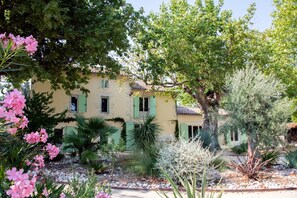 A building with a yellow facade, green shutters, and a garden with various plants and flowers. - New, spacious Provençal villa | Private pool | Sleeps 10 | Peaceful countryside (Verquières)