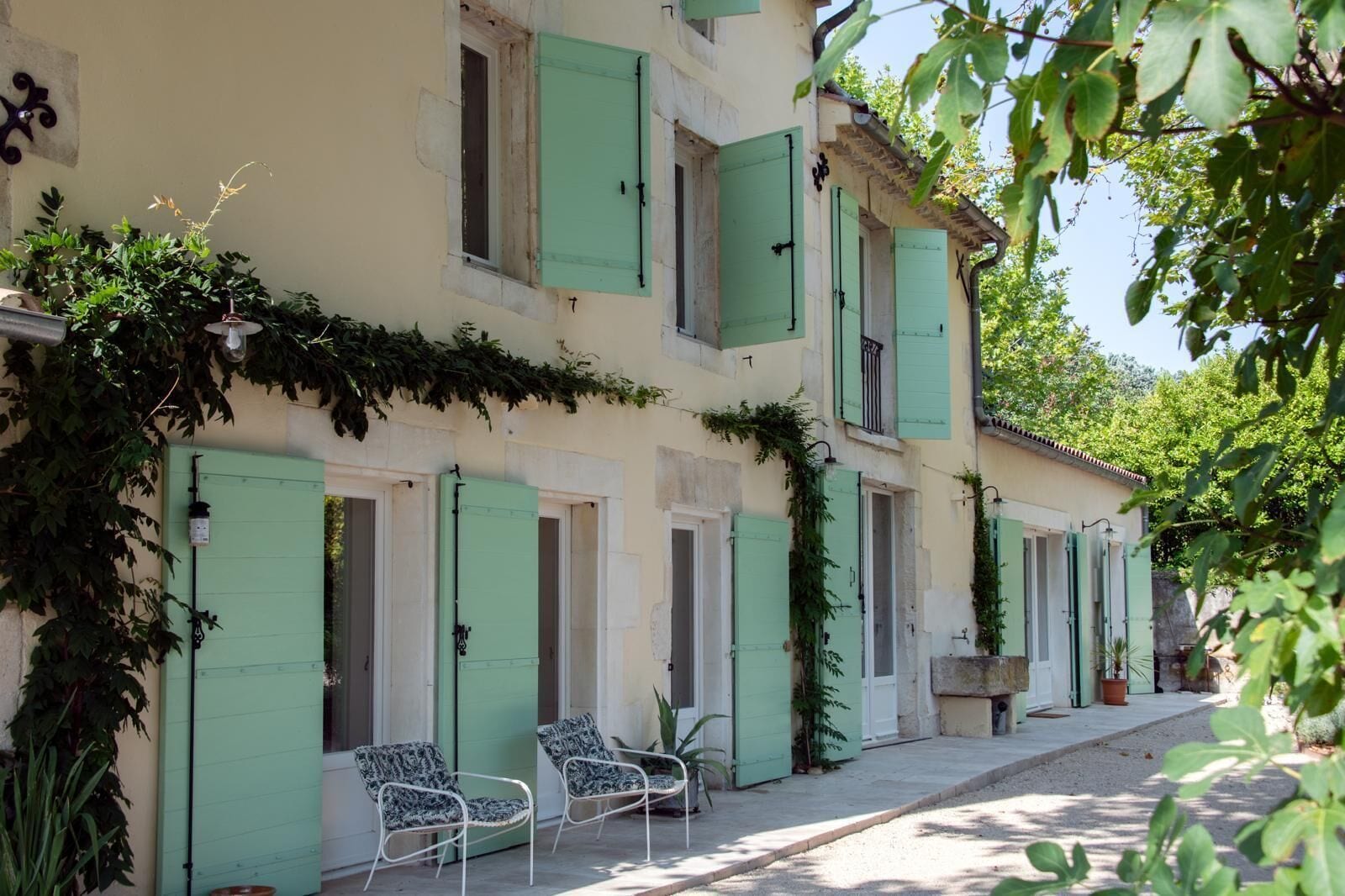 A building with multiple windows and doors, some with shutters, and a covered porch area with chairs.