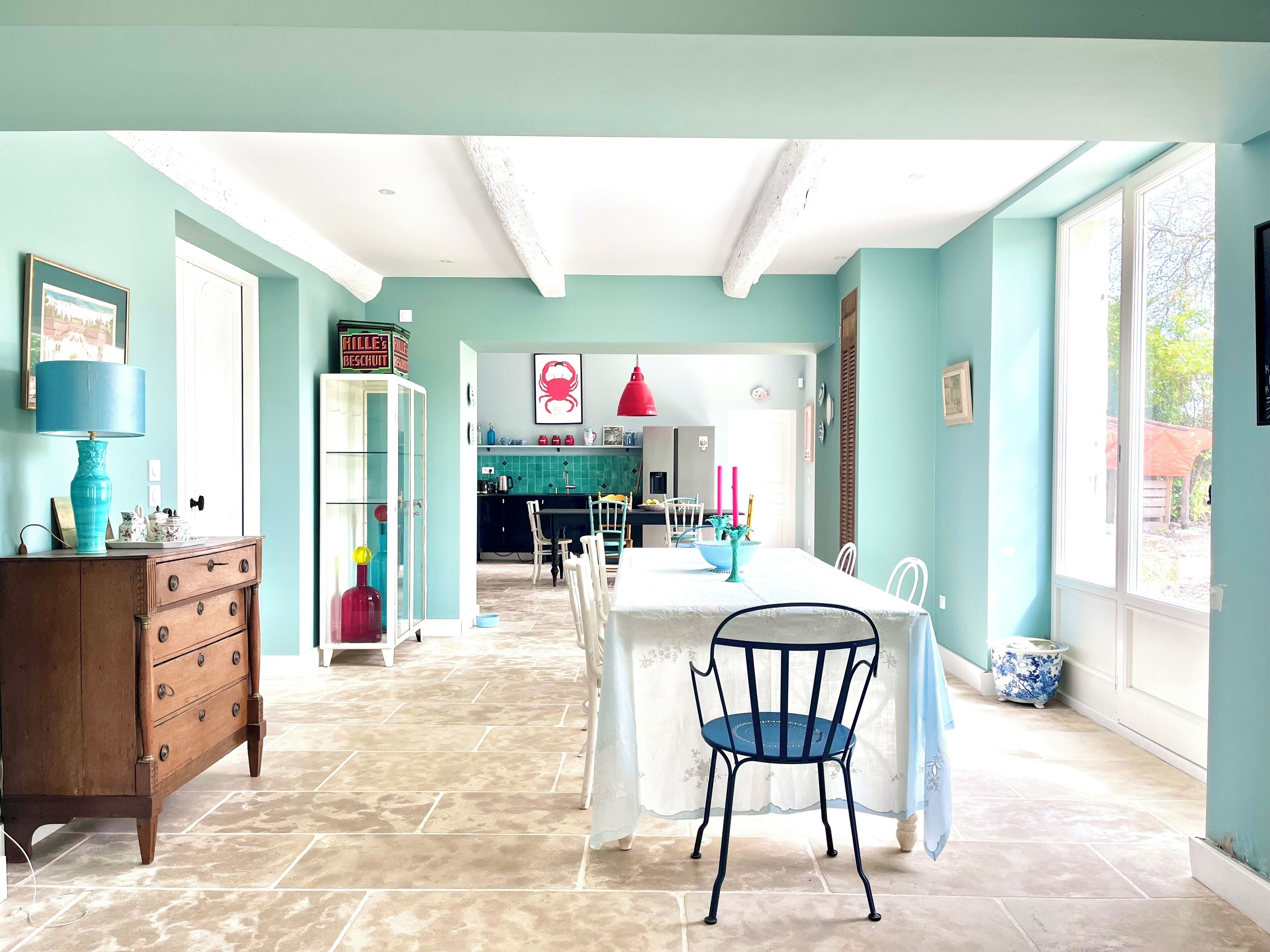 A spacious room with a dining table, chairs, a wooden cabinet, and a kitchen area in the background.
