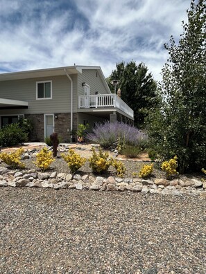 A two-story house with a balcony, surrounded by a gravel driveway and various shrubs.