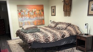Un dormitorio con una cama grande, una alfombra estampada, un cuadro en la pared y una mesita de noche con lámpara.