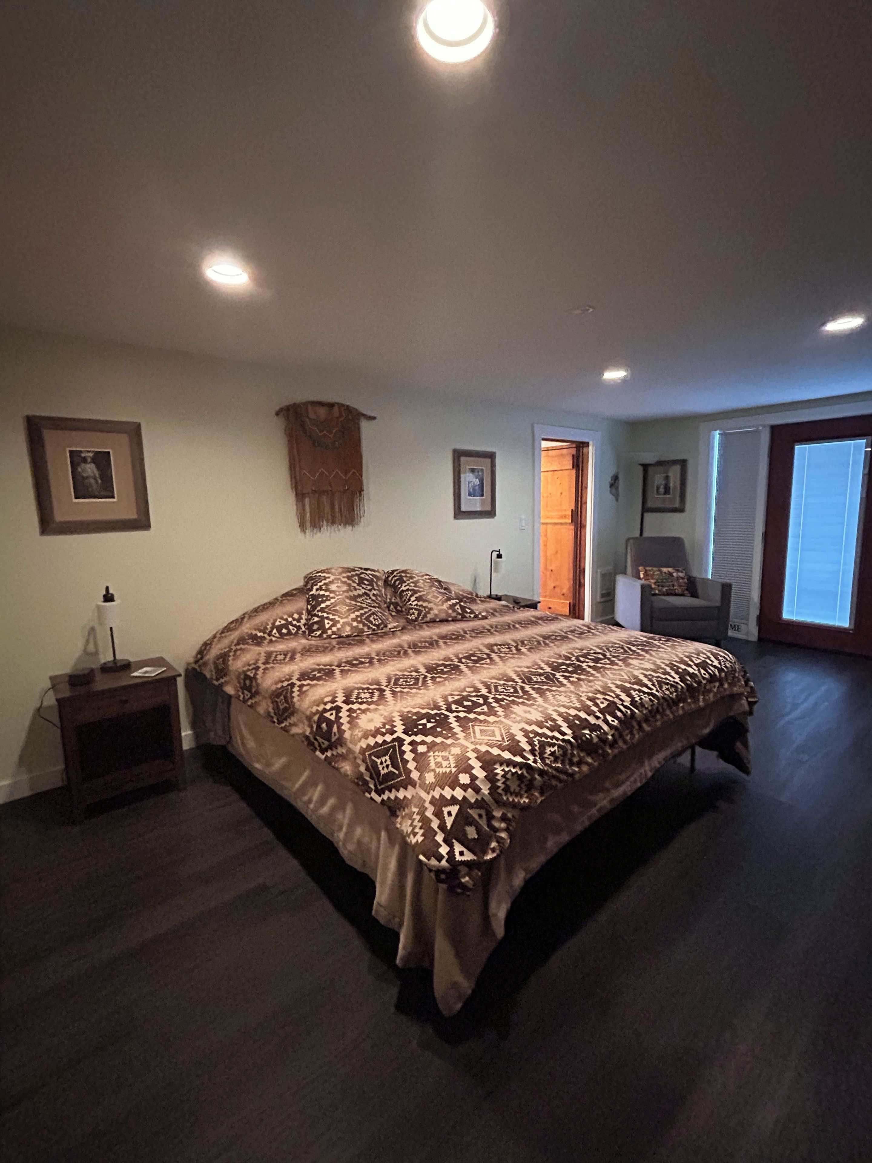 Ein Schlafzimmer mit einem großen Bett, einem Nachttisch, einem Sessel und einer Tür zu einem anderen Raum.