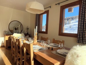 A dining area with a wooden table set for four, a mirror, and a view of a snowy landscape through windows. - Luxury half chalet 95 m2, ski-in/ski-out, panoramic view, indoor pool (Vars)