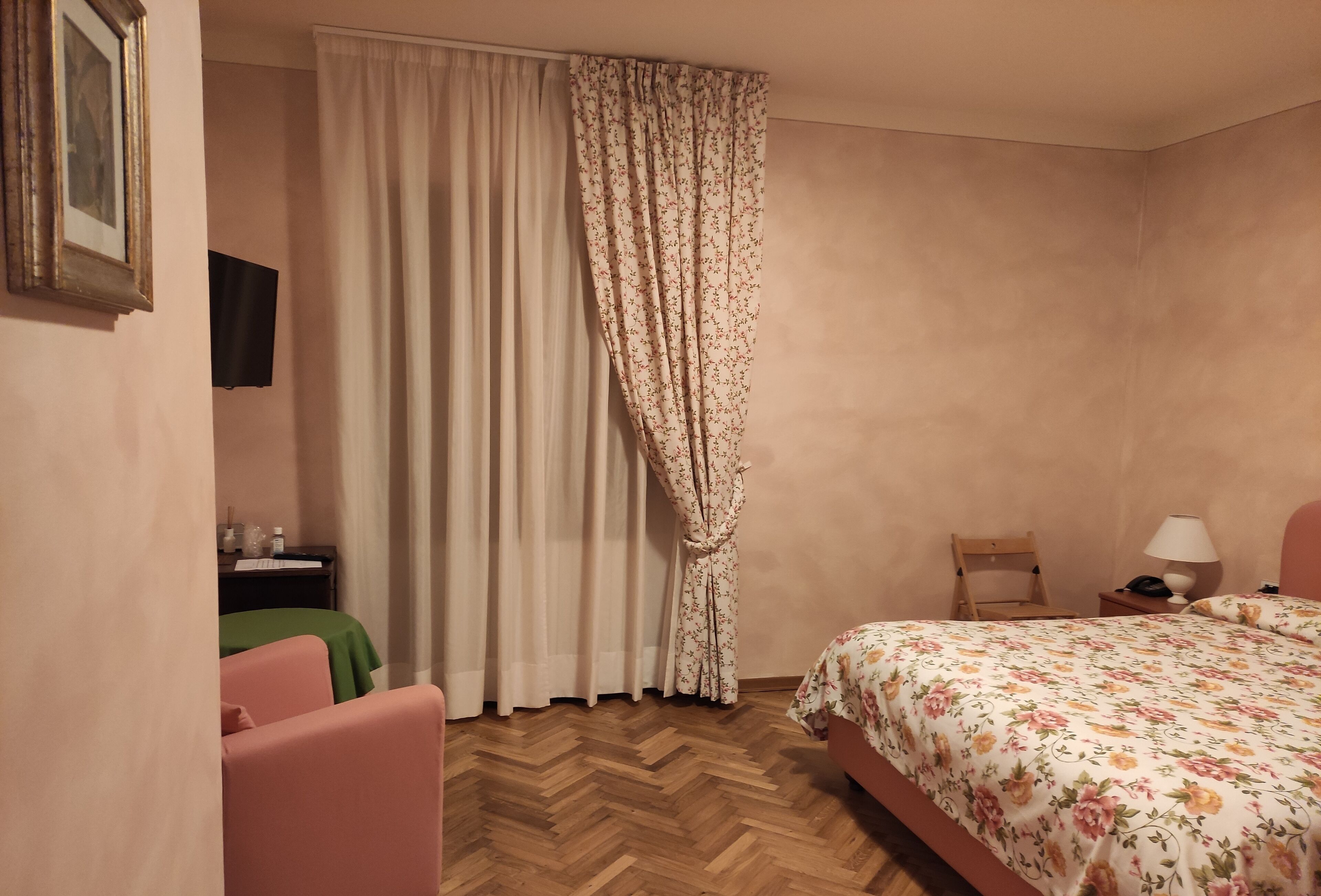 A bedroom with a bed, a chair, a nightstand, a lamp, and a wall-mounted TV.