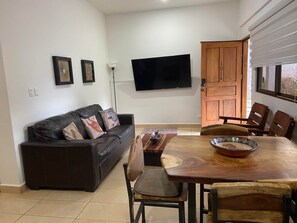 Ein Wohnzimmer mit einem dunkelbraunen Ledersofa, einem Holzesstisch und einem an der Wand befestigten Fernseher.