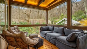 A covered outdoor seating area with a wooden deck, a wicker chair, and a gray sofa. - New! Private Waterfall! King Suite~Pet Friendly (Burnsville)