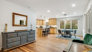 A modern kitchen with wooden cabinets, a dining area with a round table and chairs, and a large window providing a view of the outdoors. - New! Private Waterfall! King Suite~Pet Friendly (Burnsville)