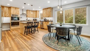 A modern kitchen with wooden cabinets, a central island, and a dining area with wicker chairs. - New! Private Waterfall! King Suite~Pet Friendly (Burnsville)