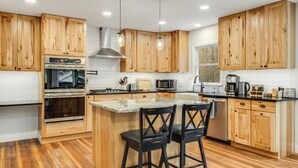 A modern kitchen with wooden cabinets, stainless steel appliances, and a central island with two bar stools. - New! Private Waterfall! King Suite~Pet Friendly (Burnsville)