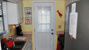 A compact kitchen with a white door, a coffee maker, a sink, and a refrigerator. - Guest Cottage 20- 2BR House- Community Pool (Myrtle Beach)