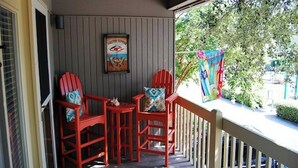A covered porch with two red Adirondack chairs and a small table, a framed picture on the wall, and a colorful banner on the railing. - Guest Cottage 20- 2BR House- Community Pool (Myrtle Beach)