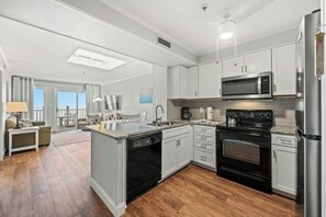 A modern kitchen with stainless steel appliances, a central island, and a view to a balcony. - Oceanfront 3BR In Shore Drive- Pelicans Landing 402 (Myrtle Beach)