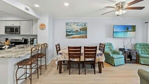 A modern kitchen with a microwave, stove, and sink. There is a dining area with a table and chairs, and a ceiling fan above. - Ocean View 3BR At Pelican's Watch 209- Pool (Myrtle Beach)