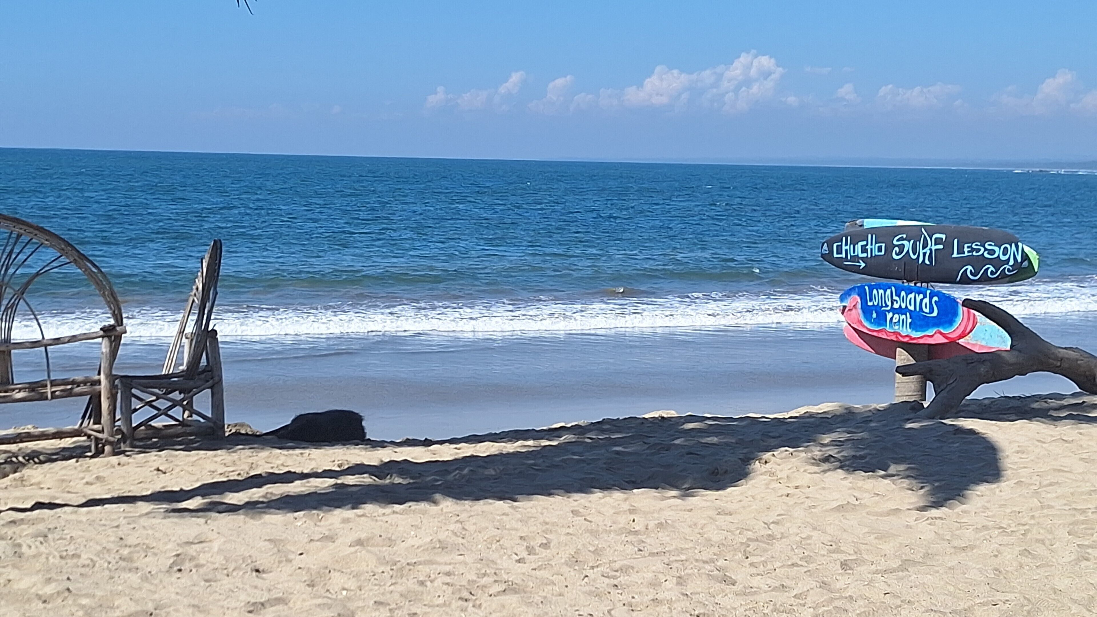 Une plage où un panneau propose des cours de surf et de la location de longboards.