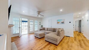 A spacious living room with a large L-shaped sectional sofa, a ceiling fan, and a view of a balcony through glass doors. - 3BR North End Beach Block Condo w/ Porch & Garage (Ocean City)