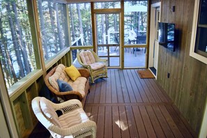 Una terraza de madera con muebles de mimbre, un televisor y vistas a otra zona de terraza con mobiliario exterior.