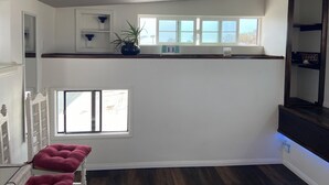 Habitació amb interior blanc, terra de fusta, finestra amb vista, una estant amb objectes decoratius i una cadira vermella.