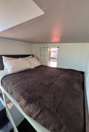 A single bed with a dark brown cover, a white headboard, and a window with a stained glass design.