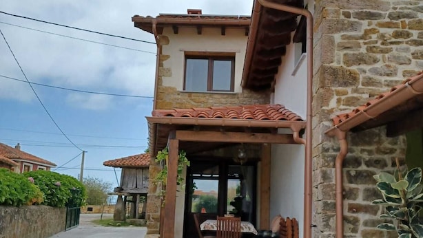 A two-story stone house with a tiled roof, a balcony, and a small outdoor seating area. - Nordés - Rural house in Lastres between the sea and the mountains (Luces)