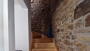 Un escalier en bois, avec un mur de pierre d’un côté et un mur blanc de l’autre.