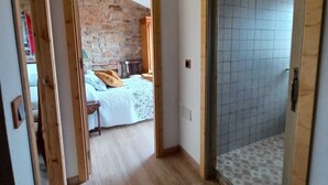 A narrow hallway with a wooden door leading to a bedroom with a stone wall and a bed with a white bedspread. - Nordés - Rural house in Lastres between the sea and the mountains (Luces)