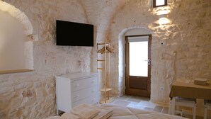 A bedroom with stone walls, a bed, a dresser, a TV, and a wooden door. - Prima Stella - Campanile Inn 
Comfortable room in historic building -Locorotondo (Locorotondo)