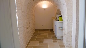A narrow hallway with a stone archway, a tiled floor, and a small kitchenette area with a green appliance. - Prima Stella - Campanile Inn 
Comfortable room in historic building -Locorotondo (Locorotondo)