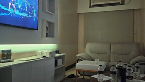 Een moderne woonkamer met een flatscreen televisie aan de muur, een plafondventilator en een beigekleurde bank.