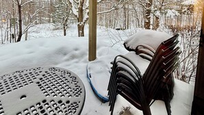 Un patio abrité, avec une table et des chaises, entouré d’arbres couverts de neige.