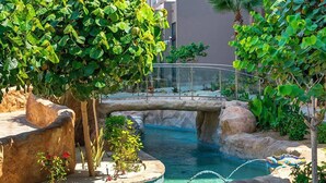Een hotel met een zwembadgedeelte, inclusief een brug, rotsformaties en verschillende planten.