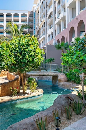 A hotel with a pool area featuring a bridge, rock formations, and various plants. - Luxury in Los Cabos (San José del Cabo)