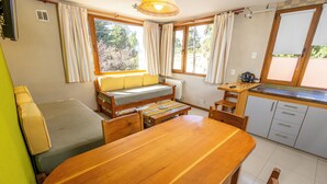 A compact room with a wooden dining table, a sofa, a small kitchen area, and a window with curtains. - Modern and quiet apartment minutes from downtown Bariloche (San Carlos de Bariloche)