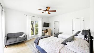 A bedroom with a bed, a sofa, a ceiling fan, a TV, and a window with curtains.