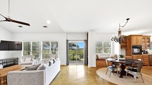 Uma sala de estar ampla com sofá, mesa de jantar com cadeiras, cozinha com armários de madeira e ventilador de teto.