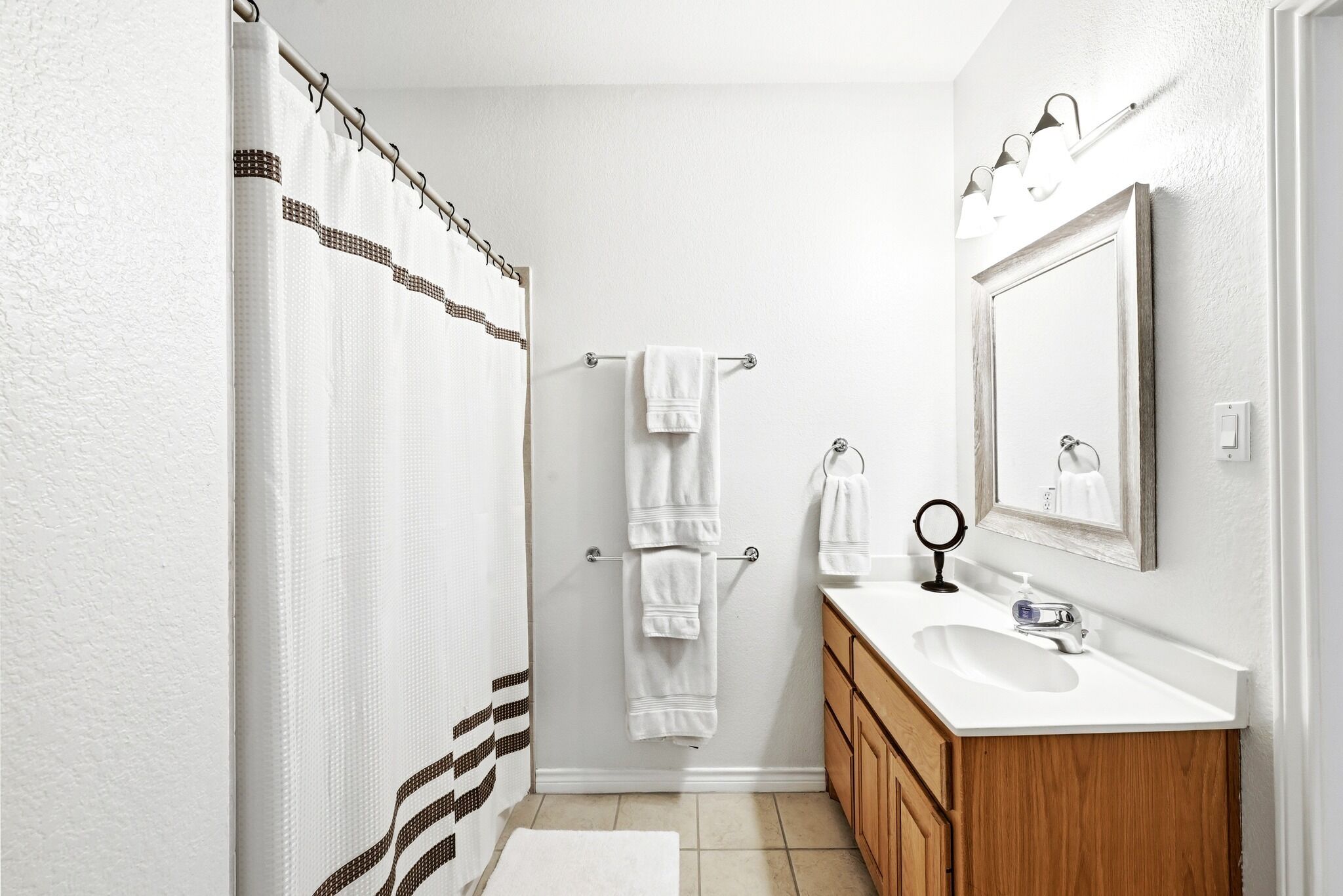 A bathroom with a shower curtain, a towel rack, a sink, a mirror, and wooden cabinets.