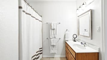 A bathroom with a shower curtain, a towel rack, a sink, a mirror, and wooden cabinets.