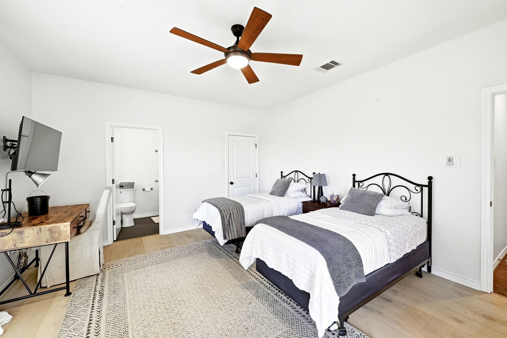 Quarto com duas camas, um ventilador de teto, uma escrivaninha com computador e televisão.