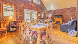 Un interior acogedor de cabaña con una mesa de comedor de madera, sillas, un sofá y una chimenea.