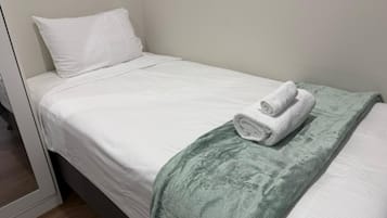 A single bed with white bedding and a green throw blanket.
