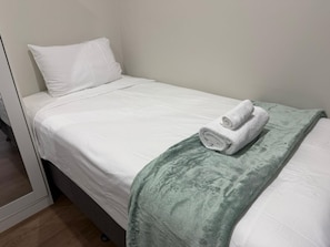A single bed with white bedding and a green throw blanket.
