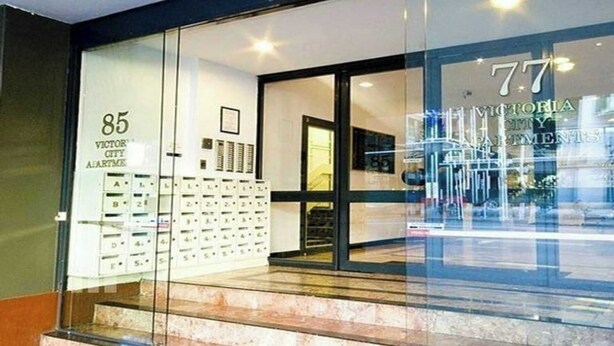 L’entrée d’un hôtel, avec une façade en verre, des panneaux indiquant le numéro des chambres et un escalier bien visible.