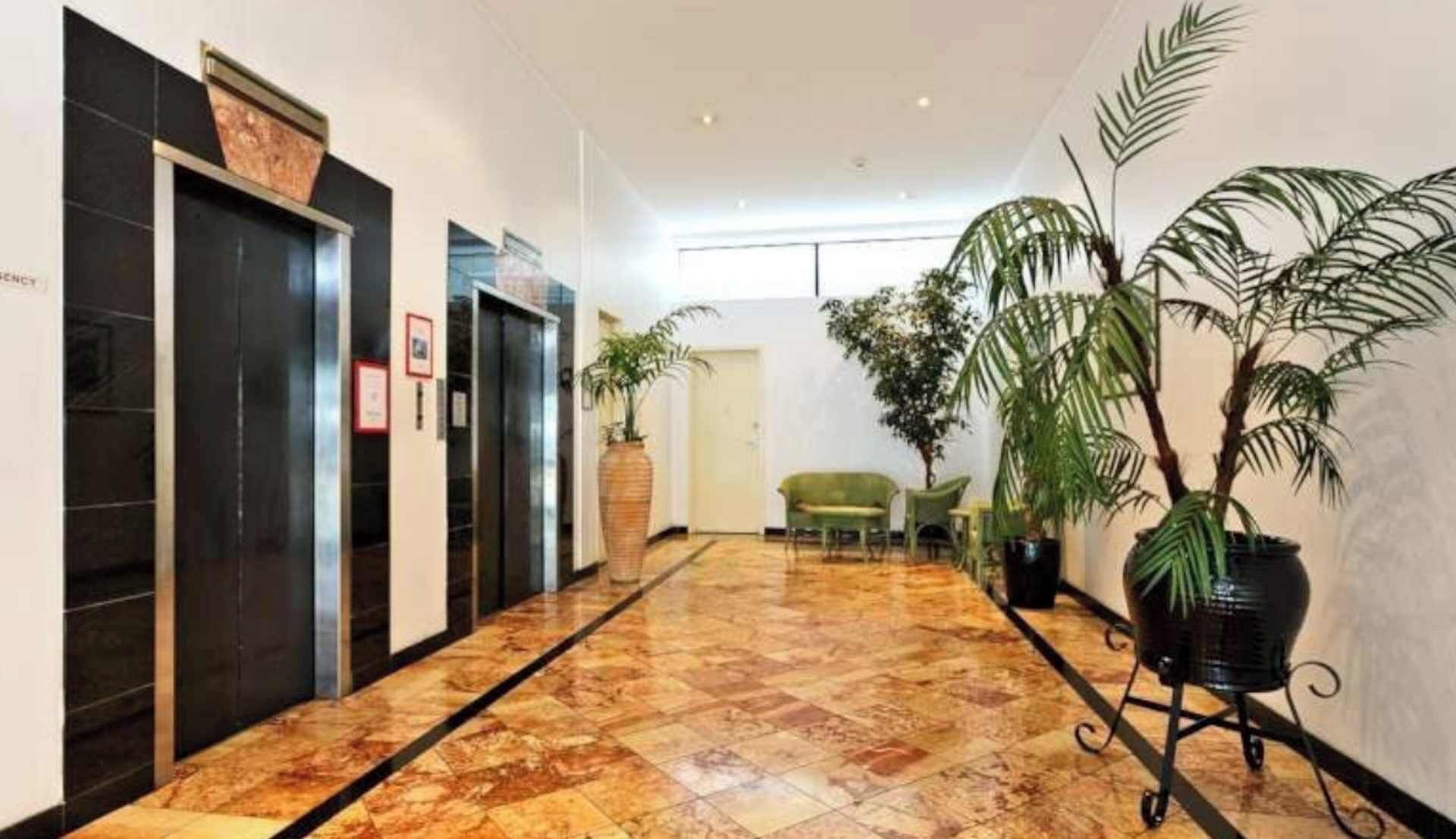 A hotel lobby with a marble floor, a reception desk, and potted plants.