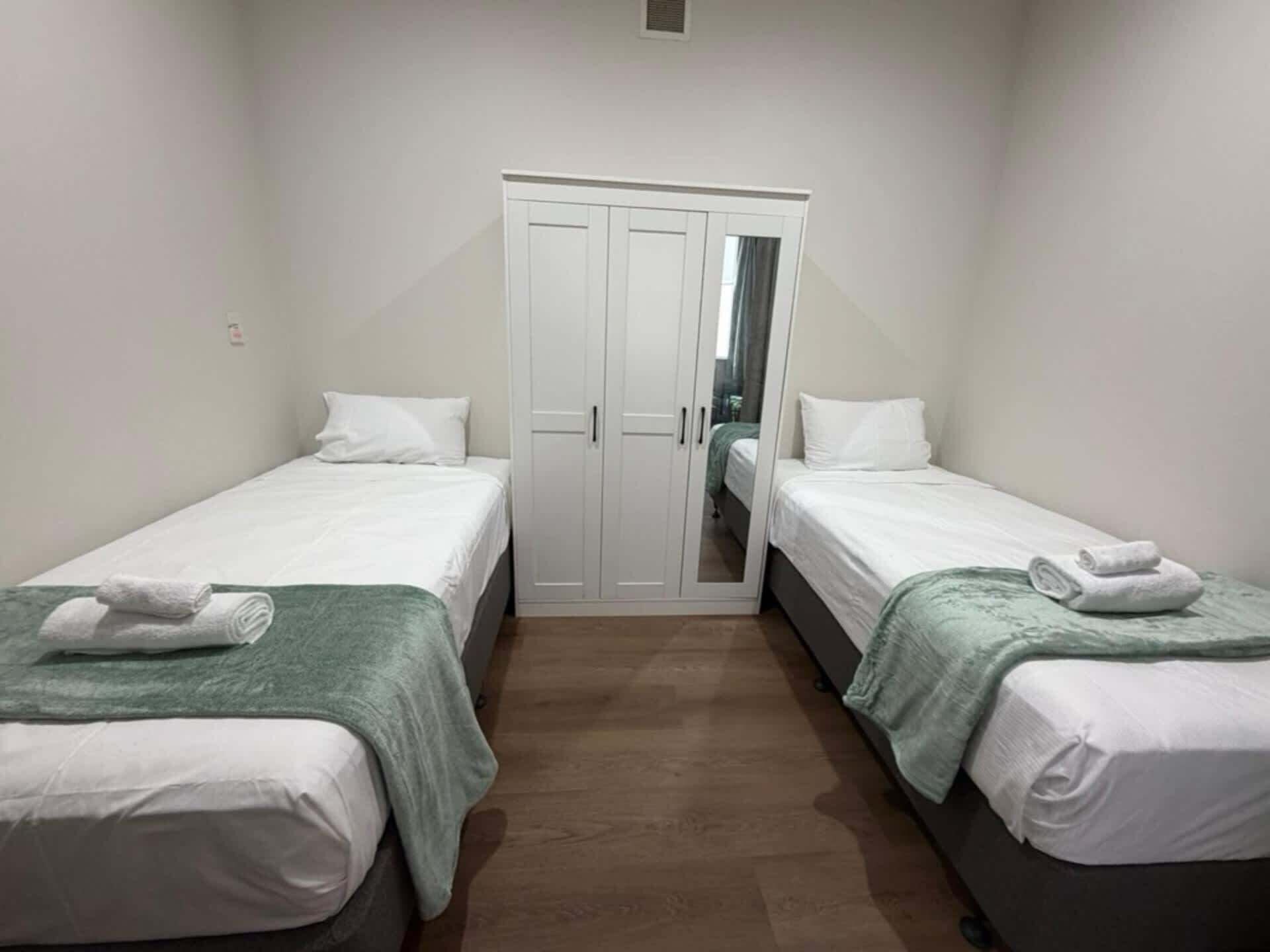 A small, clean room with two single beds, a wardrobe, and a mirror.