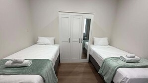 Une petite chambre propre, avec deux lits simples, une armoire et un miroir.